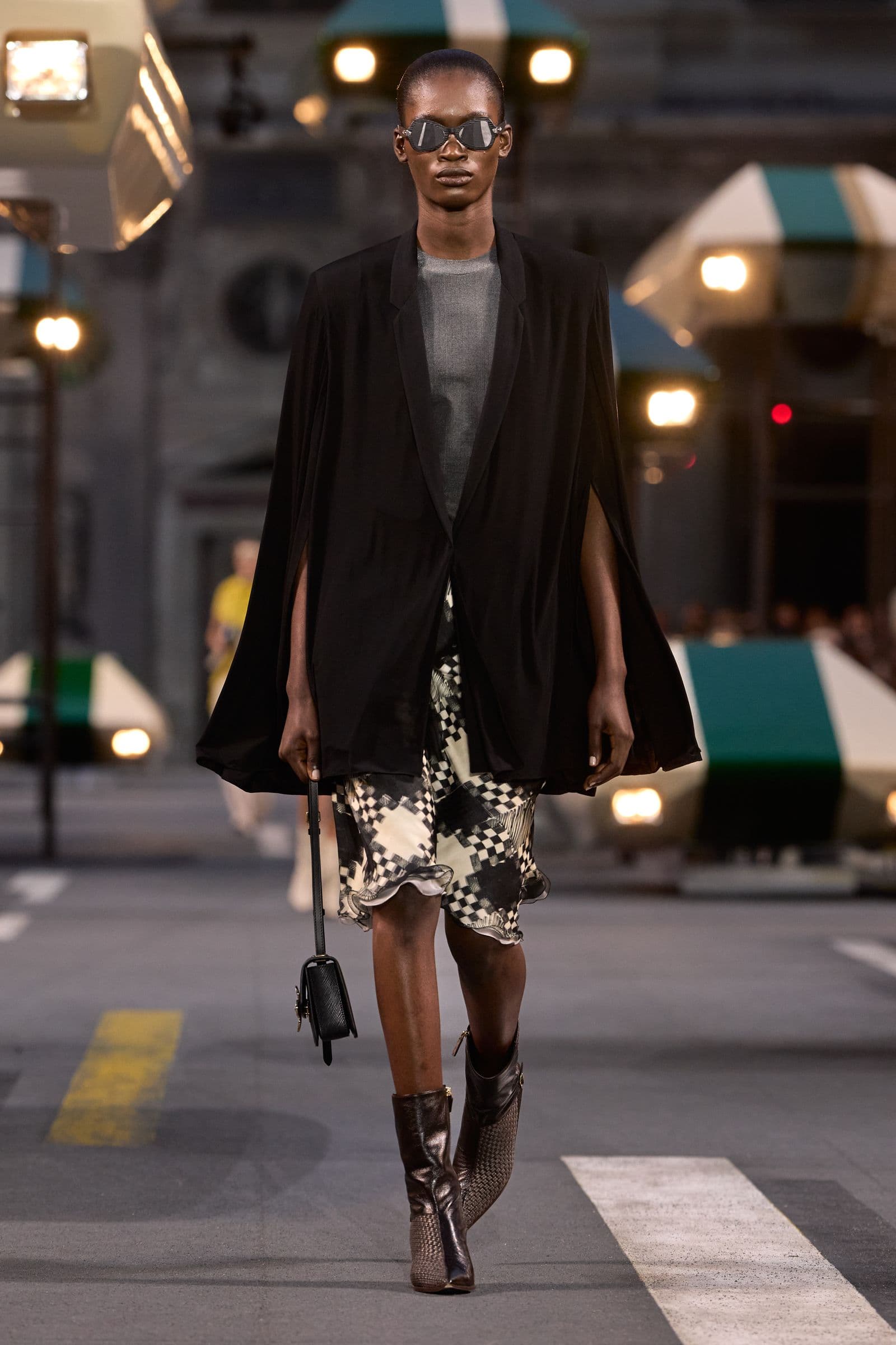 Look 43: black cape-like jacket worn over a grey top and printed skirt